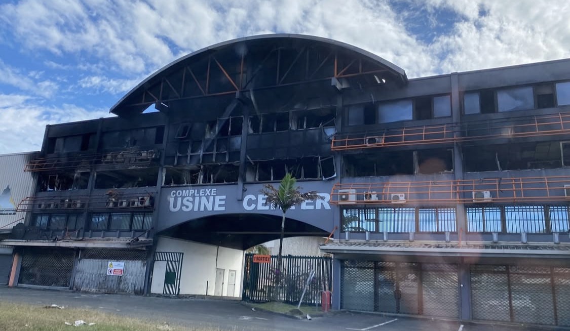 A burnt out commercial building after civil unrest, its upper floors gutted and the ground floor shuttered.