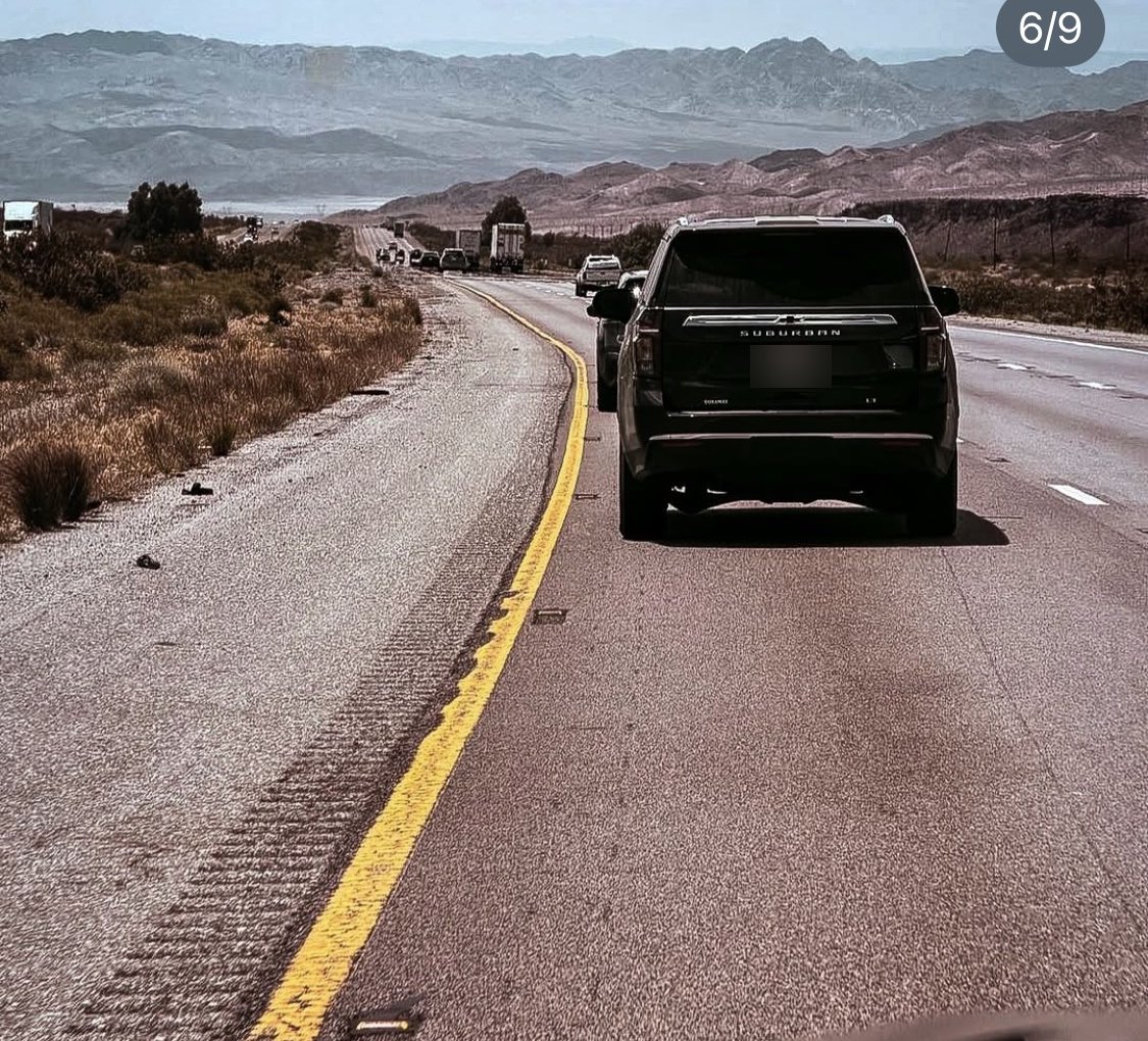A protection vehicle ahead on a desert highway in the United States, seen from the car behind it.