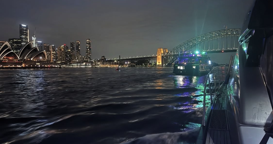 Sydney at night from the water, the Opera House and the Harbour Bridge lit across the skyline.