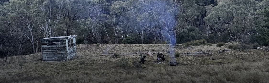 A hut and a smoking fire in a high country clearing at dusk, set up for a live training scenario.