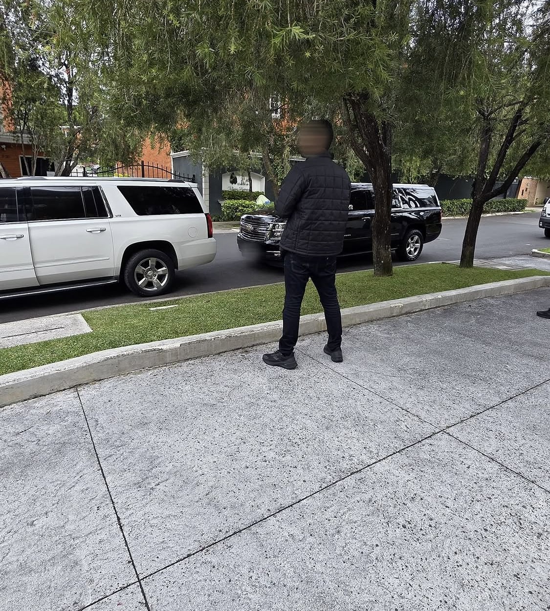 An operator holding the kerb beside a staged vehicle fleet on a residential street overseas.