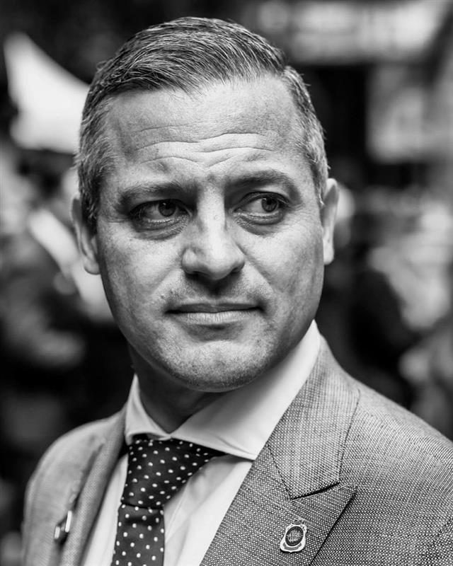 Ryan Tindall, Chief Operating Officer, in a suit and tie on a city street, photographed in black and white.