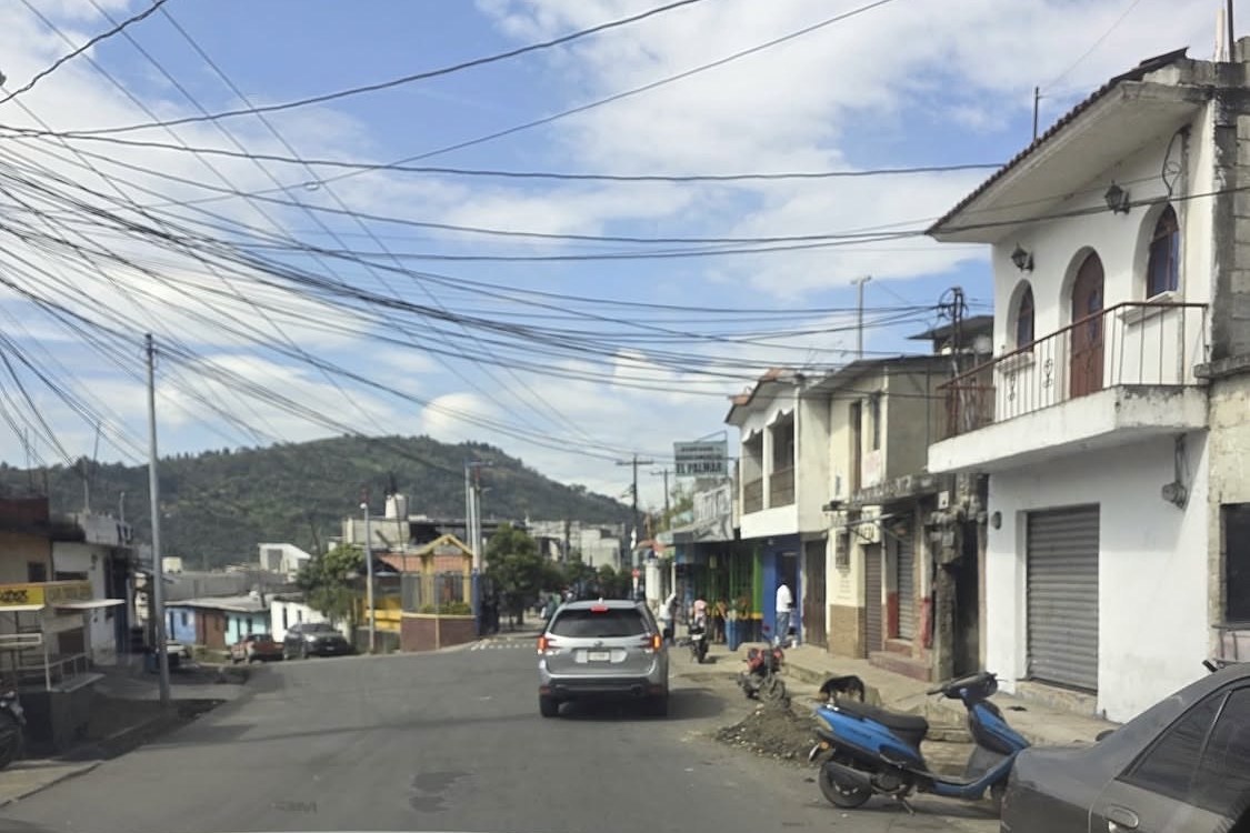 A lead vehicle ahead on a narrow street in a Central American town, seen from the following car.