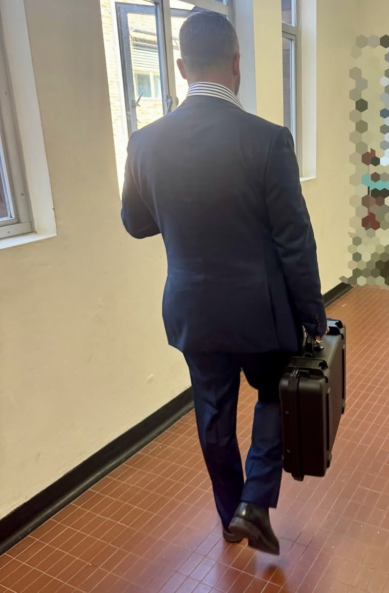 A technician carrying a hard equipment case down a corridor, on the way in to sweep a room.