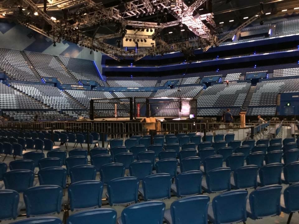 An empty arena the day before a show, seating tiers dark and the staging still being built on the floor.